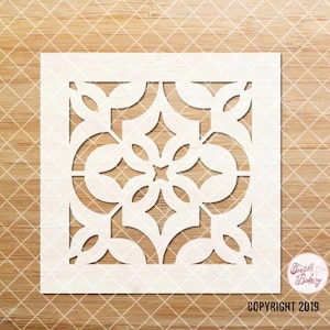 May include: White stencil with a geometric design featuring a repeating pattern of circles, leaves, and diamonds. The stencil is on a wood background. COPYRIGHT 2019.