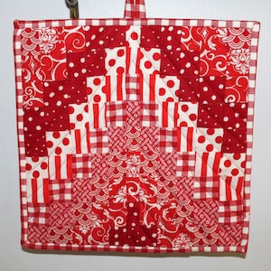 May include: Red and white patchwork pot holder with a gingham border. The pot holder is made of various red and white fabrics, including polka dots, stripes, and floral patterns.