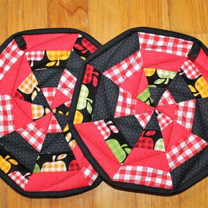 May include: Two red and black quilted pot holders with a white and red gingham pattern and apple designs.