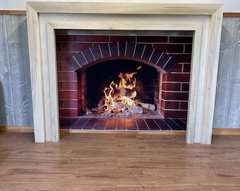 May include: A white wooden fireplace mantel with a brick surround and a roaring fire inside. The fireplace is set against a white wood panel wall.