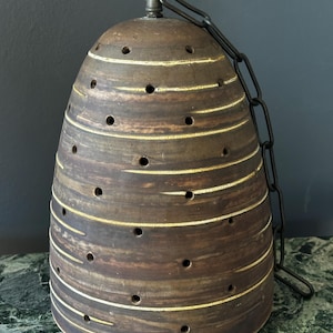 Könnte beinhalten: Eine braune Keramik-Pendelleuchte mit einer Kette, die ein strukturiertes, gestreiftes Design und kleine Löcher aufweist.