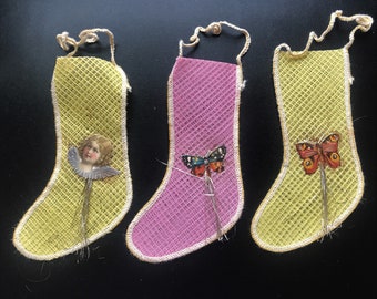 May include: Three vintage Christmas stockings with different decorations. One stocking is yellow with an angel, one is pink with a butterfly, and one is yellow with a butterfly.