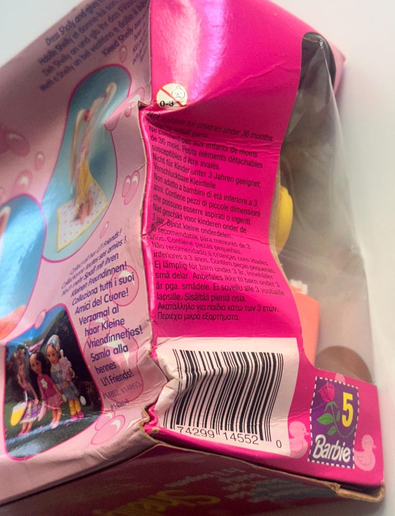 May include: A pink Barbie product packaging box featuring a barcode, a small yellow warning icon for children under 36 months, and multi-language text including 'Collect all her Lil' Friends!' and 'Barbie' with a number 5 logo.