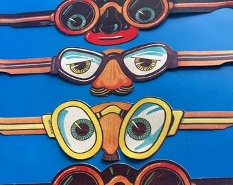 May include: A selection of vintage paper novelty glasses with attached orange and black striped bands. Each pair features large, cartoonish eyes, a nose, and a mouth in various colours, including red, orange, yellow, and green. The background is a solid blue.