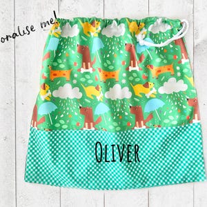 May include: Green drawstring bag with a pattern of cartoon dogs, umbrellas, and clouds. The bottom section has a green and white checkered pattern with the name "OLIVER" printed in black. The text "Personalise me!" is written in black.
