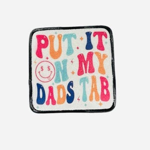 May include: A white square patch with a black border. The patch has a colorful design with the text "PUT IT ON MY DADS TAB" and a smiley face with dollar signs for eyes.