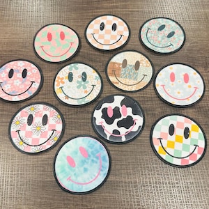 May include: Ten different smiley face patches with various patterns, including checkered, floral, and cow print. The patches are all round and have a black outline.