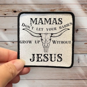 May include: White iron-on patch with black text and a black and white cow skull graphic. The text reads "Mamas Don't Let Your Babies Grow Up Without Jesus".