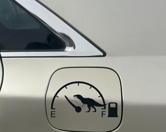 May include: A white car with a black dinosaur fuel gauge sticker. The gauge shows the needle pointing to empty, with the dinosaur running towards the full mark. The sticker says "E" for empty and "F" for full.