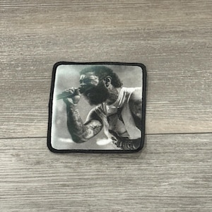 May include: Black and white photo of a man singing into a microphone. He is wearing a tank top and has a beard. The photo is printed on a black patch.
