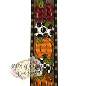 May include: A vertical rectangular sign featuring five stacked pumpkins with varied patterns including red stripes, black and white spots, orange stripes, black and white checks, and solid orange. The border is black and gold checkered. Text reads Wild Whimsy Wood Decor.