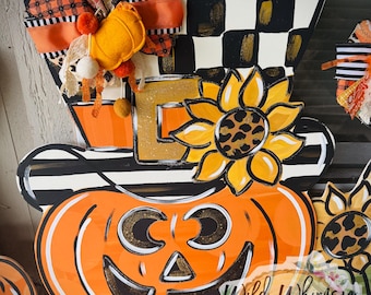 Puede incluir: Decoración de madera con temática de Halloween que presenta una calabaza sonriente, un girasol con estampado de leopardo y un sombrero de copa con un patrón de cuadros blancos y negros. La decoración incluye cintas naranjas y negras y el texto "Wild Whimsy Wood Decor".