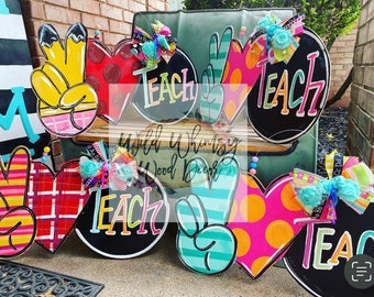 Può includere: Una collezione di appendiporta in legno colorati con la parola "Teach" su di essi. Gli appendiporta sono decorati con diversi motivi, tra cui strisce, pois e quadri.
