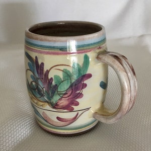 Puede incluir: Una taza de cerámica con fondo amarillo y un diseño floral colorido. La taza tiene un asa marrón y un borde blanco.