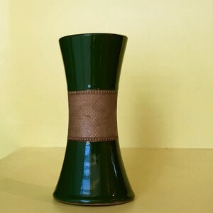 Può includere: Un vaso in ceramica verde scuro con una fascia marrone intorno al centro. Il vaso ha una base larga e un collo stretto.