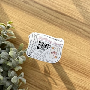 May include: A white sticker with a black outline of a newspaper headline that reads "Breaking News: Local Mom Searches For Where The Men Get The Audacity." The sticker features a small illustration of binoculars and stars.