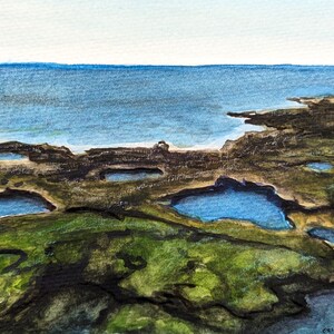 May include: Watercolor painting of a coastal landscape with a blue ocean in the background and a rocky foreground with several small blue pools of water. The painting is signed "Erica Jarvey '24" in the lower right corner.