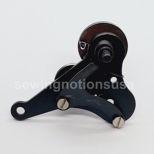 May include: Black metal sewing machine part with a curved arm and two small screws. The part has a circular gear with a small metal rod extending from the center.