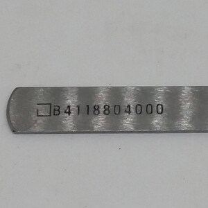 May include: A silver metal ruler with a black marking that reads "B4118804000".