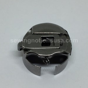 May include: A silver metal bobbin case for a sewing machine. The bobbin case has a spring and a metal latch.