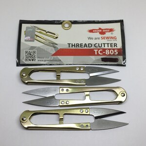 May include: Three gold thread cutters with silver blades. The cutters are packaged with a black and red card that reads "Golden Eagle We are Sewing Since 1978 Thread Cutter TC-805".