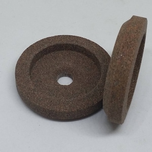 May include: Two brown grinding wheels with a center hole. The wheels are made of a coarse abrasive material.