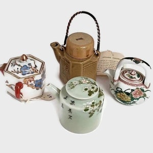 Pode incluir: Quatro bules de chá de cerâmica em miniatura com intrincados desenhos florais. Os bules são de várias cores, incluindo branco, verde, marrom e rosa. Os bules têm formas e tamanhos diferentes, e cada um tem um design único.