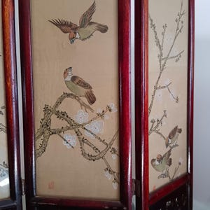 May include: A wooden folding screen with panels depicting hand-painted birds and floral branches. The birds are in shades of brown, tan, and green, against a beige background. The frame is a deep red colour.