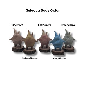 May include: Five ceramic figurines in different colors, each with a star-shaped head and a rounded body. The colors are tan, red, green, yellow, and blue. The figurines are standing on small wooden bases. The text "Select a Body Color" is at the top of the image.