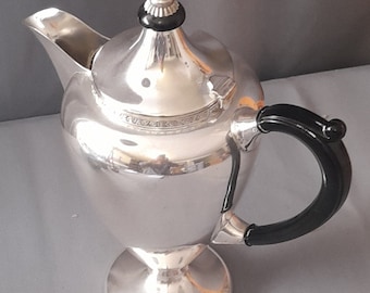 Op de afbeelding: Zilveren theepot met een zwarte handgreep en een zwarte knop op de deksel. De theepot heeft een rond lichaam en een uitlopende basis.