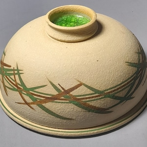 May include: A ceramic dome with a green glass top. The dome is decorated with a pattern of brown and green lines.