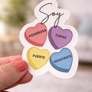 May include: A sticker with a white border and the word "Soy" in cursive. The sticker has four heart-shaped elements with the words "Poderosa", "Capaz", "Fuerte", and "Resistente" in red, purple, yellow, and blue.