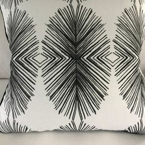 May include: A white throw pillow with a black geometric pattern. The pattern features a series of radiating lines that create a starburst effect.