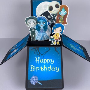 May include: A pop-up birthday card with a blue background and a black frame. The card features characters from the Nightmare Before Christmas and the movie Up. The card reads 'Happy Birthday' in yellow text. The card has a bouquet of purple flowers in the bottom left corner.