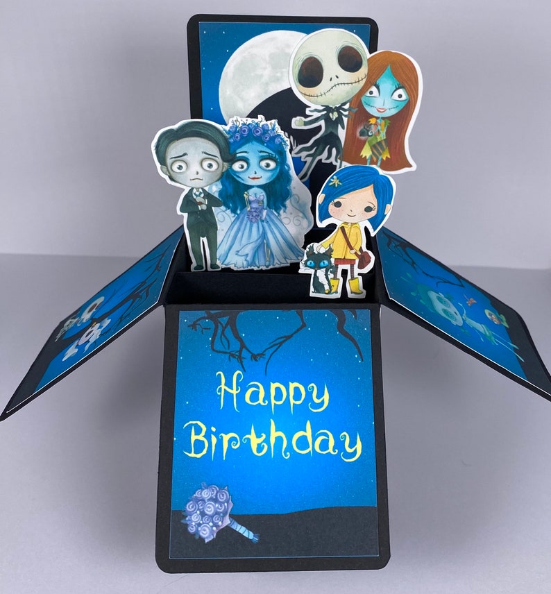 May include: A pop-up birthday card with a blue background and a black frame. The card features characters from the Nightmare Before Christmas and the movie Up. The card reads 'Happy Birthday' in yellow text. The card has a bouquet of purple flowers in the bottom left corner.