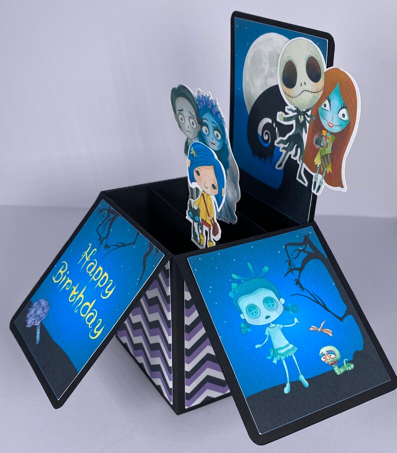May include: A black pop-up card with a blue, white, and black chevron pattern on the inside. The card is open and has a pop-up scene with characters from the Nightmare Before Christmas and Corpse Bride movies. The card says 'Happy Birthday' on the front.