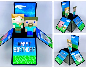 May include: A pop-up birthday card featuring Minecraft characters. The card is black with a green grass base and a blue sky background. The card says "Happy Birthday" in pixelated letters.