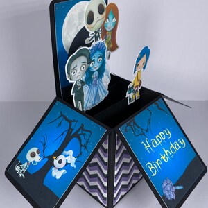 May include: A black and blue pop-up card with a chevron pattern on the inside. The card features characters from the Nightmare Before Christmas and Corpse Bride movies. The card is open and the inside reads 'Happy Birthday'.