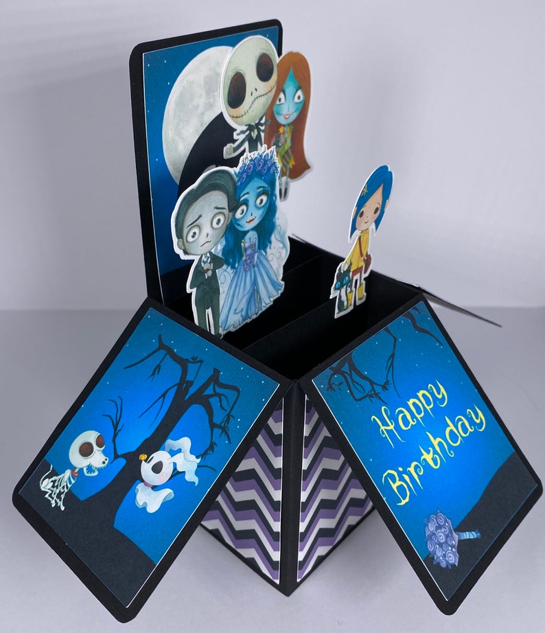 May include: A black and blue pop-up card with a chevron pattern on the inside. The card features characters from the Nightmare Before Christmas and Corpse Bride movies. The card is open and the inside reads 'Happy Birthday'.