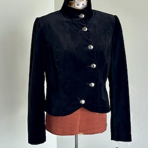 May include: A black velvet jacket with a high collar and silver buttons. The jacket has long sleeves and is displayed on a mannequin. The design is classic and elegant, suitable for formal wear. The jacket is approximately 60 cm in length.