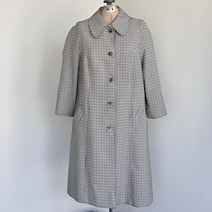 May include: A knee-length coat featuring a black and white micro-check pattern, a rounded collar, and five front buttons. The coat has three-quarter length sleeves and two side pockets, displayed on a mannequin to show its structured silhouette.