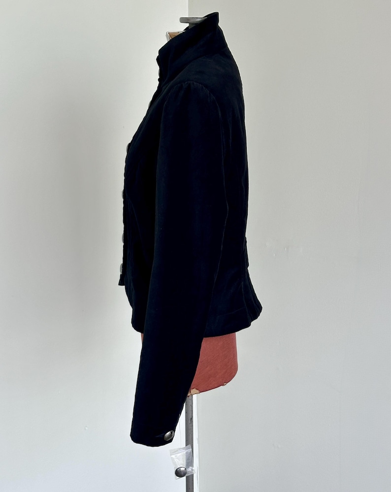 May include: A black jacket with a high collar and button details. The jacket has long sleeves and a fitted waist. The fabric appears to be a soft, velvety material. The jacket is displayed on a mannequin.