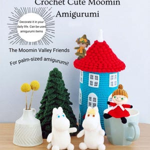Peut inclure: Ensemble d'amigurumis Moomin au crochet comprenant deux figurines blanches, un personnage en robe rouge, un personnage au chapeau vert, une tour bleue à toit rouge, un sapin au crochet vert et un vase blanc avec des fleurs jaunes, avec texte.