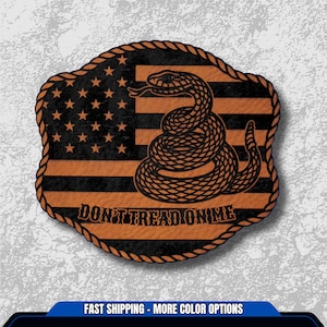 May include: A wooden plaque featuring the American flag design with a coiled snake and the words "DON'T TREAD ON ME". The plaque has a rope-like border and is in shades of black and orange.