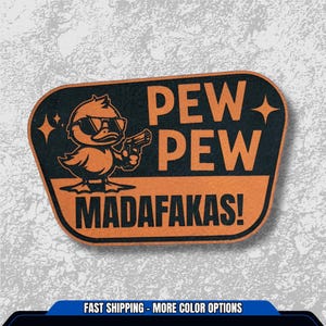 May include: An orange and black sticker featuring a cartoon duck wearing sunglasses and holding a gun. The text "PEW PEW MADAFAKAS!" is displayed in orange block letters.
