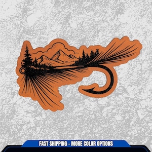 May include: An orange sticker in the shape of a fishing hook, featuring a black mountain and forest landscape. The hook design includes a detailed illustration of a mountain range, trees, and a river. The sticker has the text "FAST SHIPPING - MORE COLOR OPTIONS".