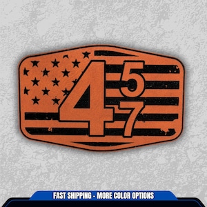 May include: An orange and black patch with the number "457" overlaid on a distressed American flag design. The patch has a rectangular shape with rounded corners and a textured appearance.
