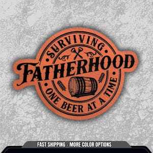 May include: An orange circular patch with the words "SURVIVING FATHERHOOD" and "ONE BEER AT A TIME" in black. The design includes a beer barrel, crossed axes, and wheat stalks. The patch has a textured appearance.