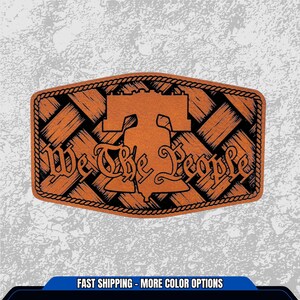 May include: A rectangular, brown leather belt buckle with a woven design and a black border. The Liberty Bell is in the center, with the words "We The People" in a decorative font.