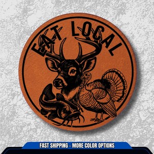 May include: Round, orange-brown graphic with the words "EAT LOCAL" in black, encircling a black illustration of a deer, turkey, and catfish. The design is likely for a sticker or patch, promoting local food.